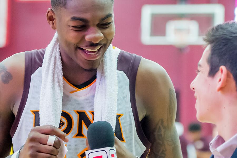 A male student interviews an Iona basketball player on the court after a game