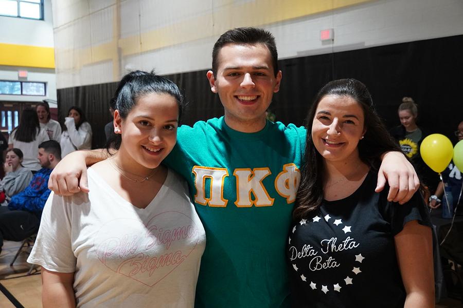 Two sorority members and a fraternity member smile at the involvement fair.