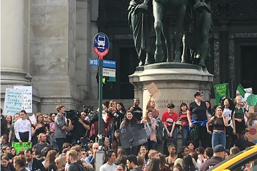 Demonstrators gather in a crowd in front of a statue to raise awareness for climate change.