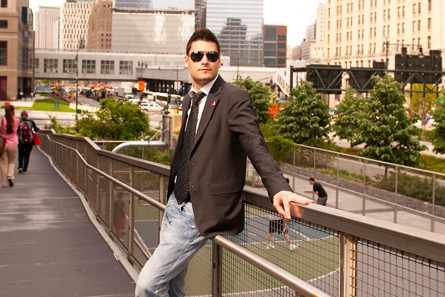 A law student in a jacket and tie with jeans and sneakers leans against a railing in downtown Manhattan.