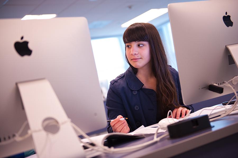 A student works at a computer and looks up and smiles.