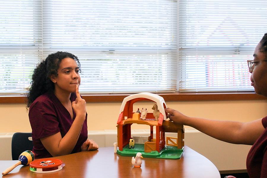 Two CSD students practice and one points to her mouth to demonstrate how the shape should feel.