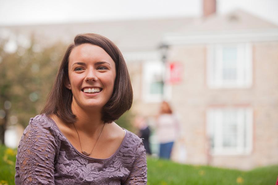 A student in the education department sits outside and smiles.