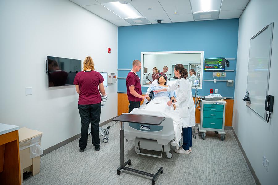 Two nursing students and a professor practice on a mannequin in the lab.