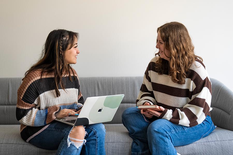 Two students work on a couch in LaPenta School of Business and smile.