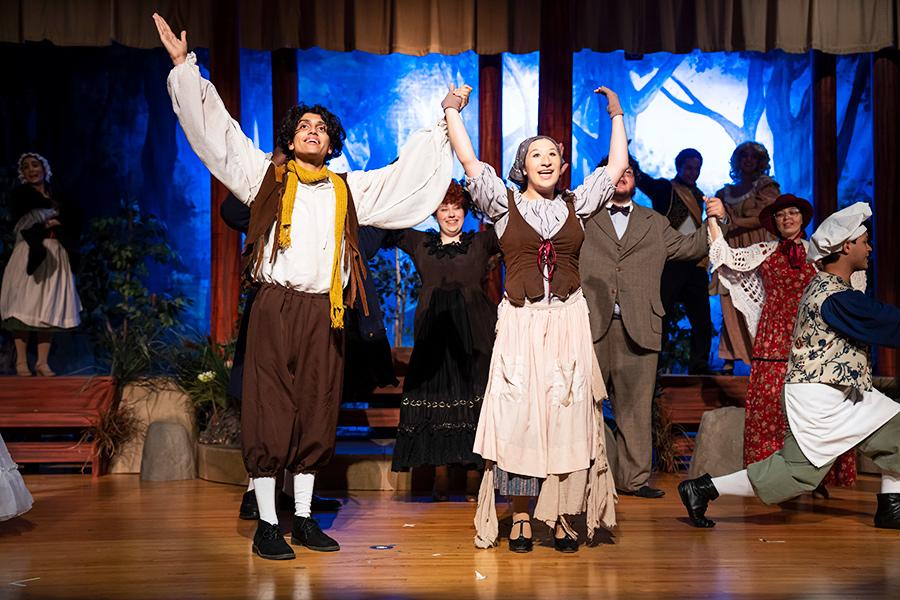 Two students sing and raise their arms in a performance of Into the Woods.