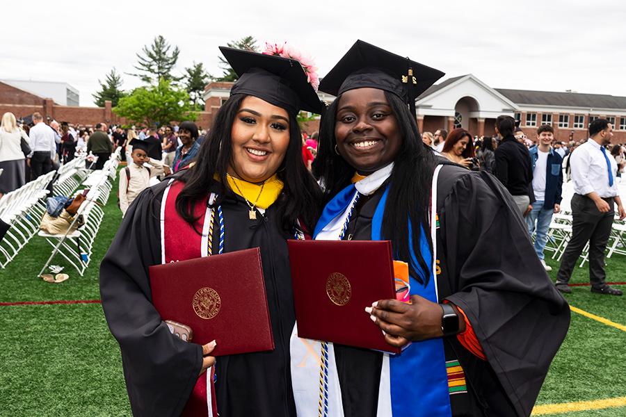 Two students hold their degrees and smile. 