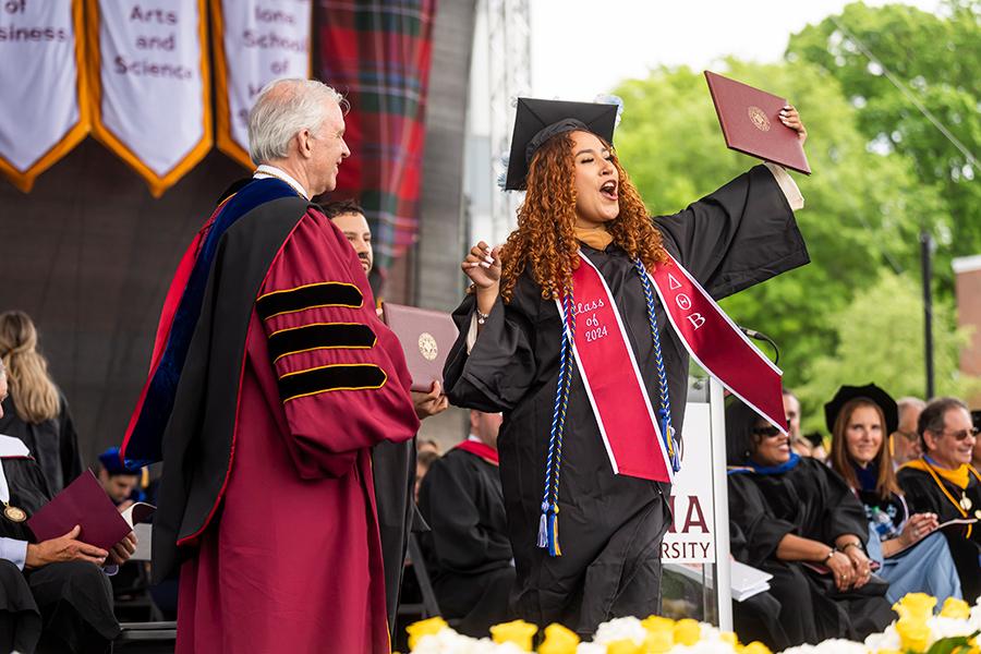 A student cheers to the crowd as she holds her degree.