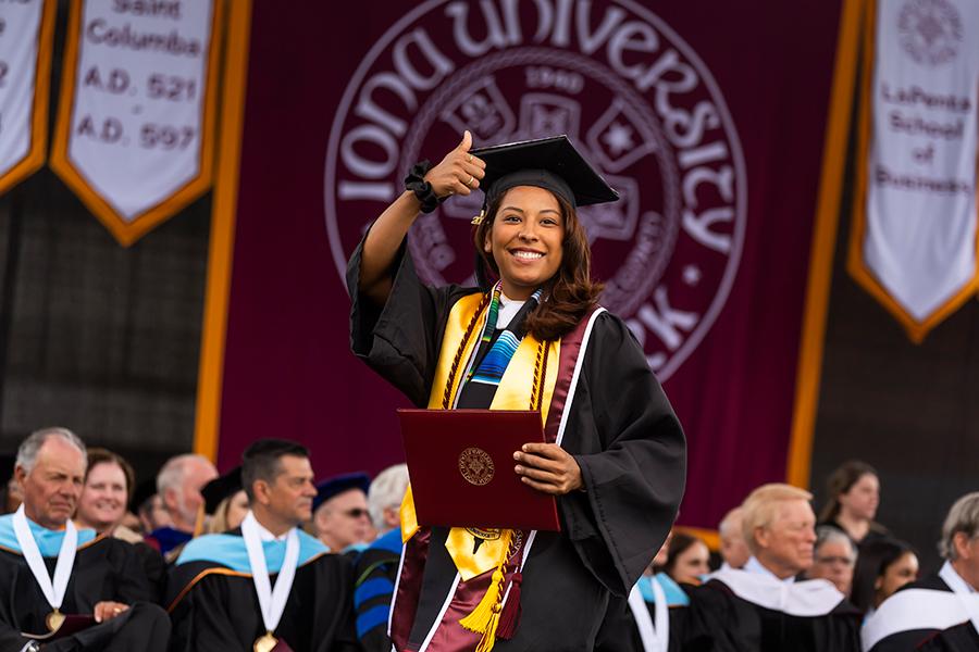 A student crosses the stage and gives a thumbs up at the 2024 Commencement ceremony.