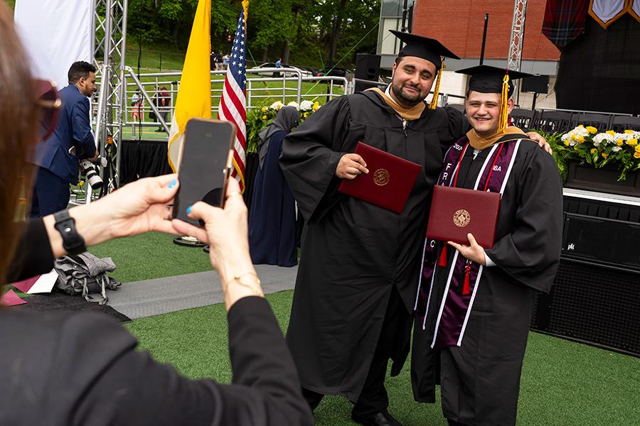Two graduates hold their degrees and smile for a photo.