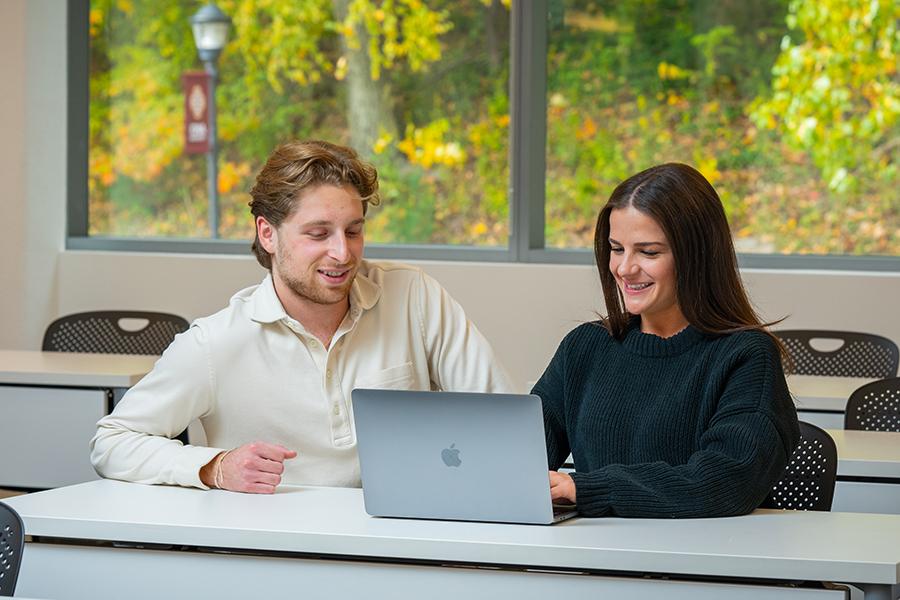 Two graduate students work on a laptop in the LaPenta School of Business.