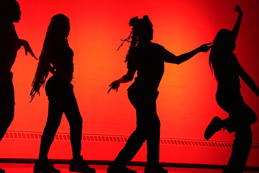 Four BSU members dance on stage with a red background.