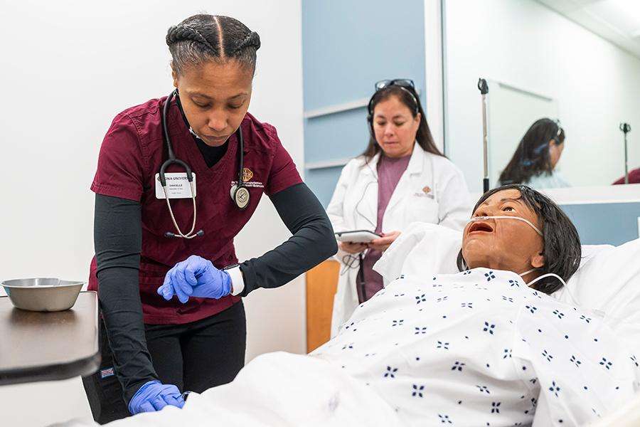 A graduate nursing students checks the pulse on a nursing mannequin.