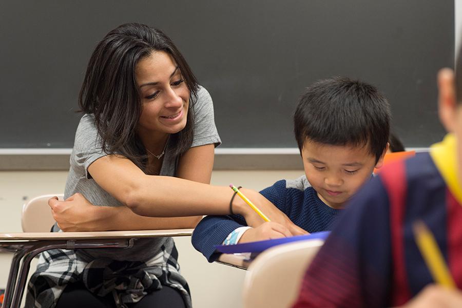 A student teacher helps a young student in a classroom.