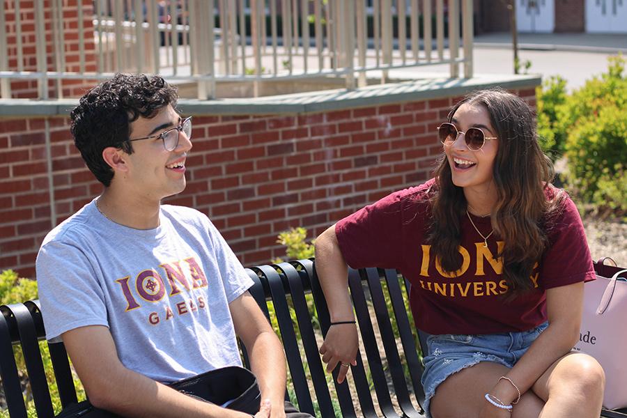 Two transfer students smile and talk on a bench.