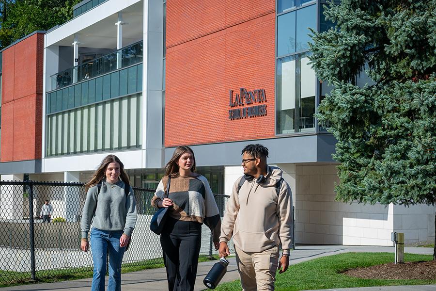 Three students walk by the LaPenta School of Business on a sunny day.