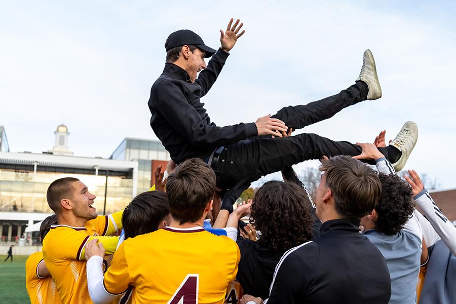 The men's soccer team lifts up their coach in victory.