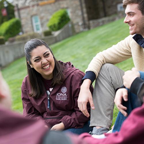 Students sit and talk on the east lawn. One student wears a Gael Guides jacket.