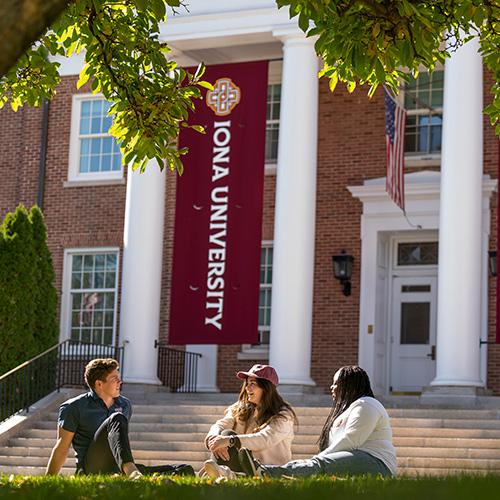 Three students sit and talk near McSpedon Hall.