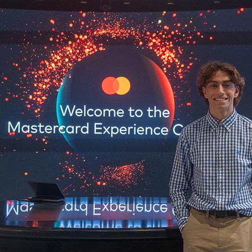 An Iona student in front of the Welcome to Mastercard sign.