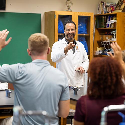 A chemistry teacher points to a student in class and smiles.