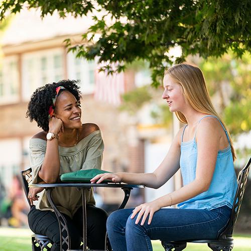 Two students talk outside on a sunny day.