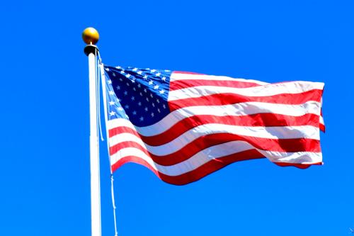 The American flag blows on the quad blows in the breeze in front of a blue sky.