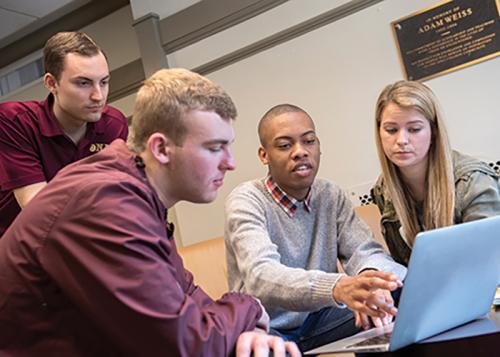 Students gather around a laptop in the Ryan Library.