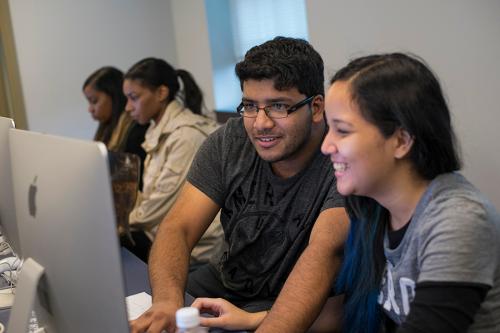 Two students work enthusiastically at an iMac in the computer lab.