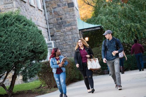 Three gaels walk by Doorley Hall on a fall day.