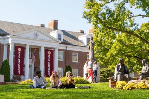 Three students sit outside near McSpedon Hall on a sunny day.