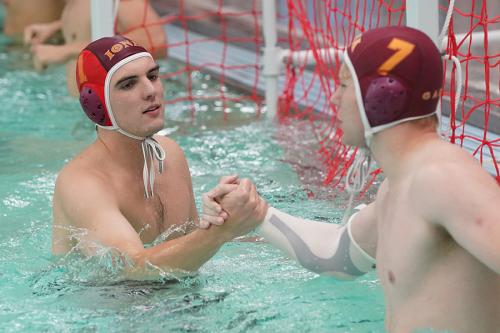 Two men's water polo players high five at a game.