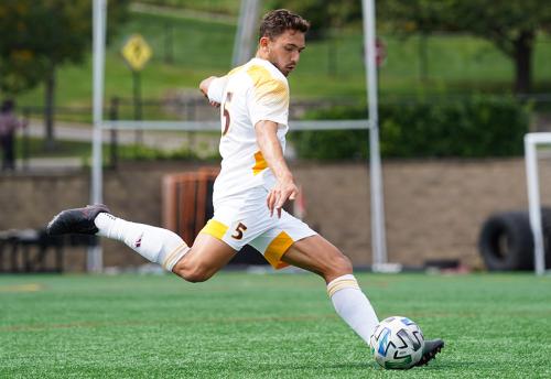 A member of men's soccer kicks the ball down field.