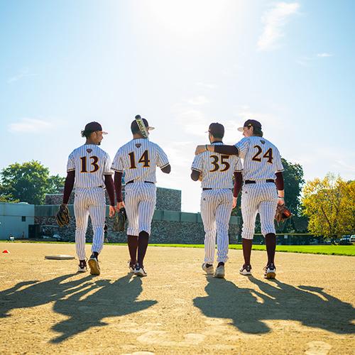 Four members of the baseball team walk off the field on a sunny day.