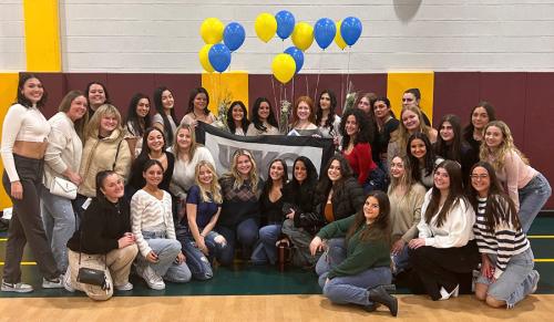 The 2024 members of Psi Kappa Theta in Mulcahy Gym with a banner and balloons.