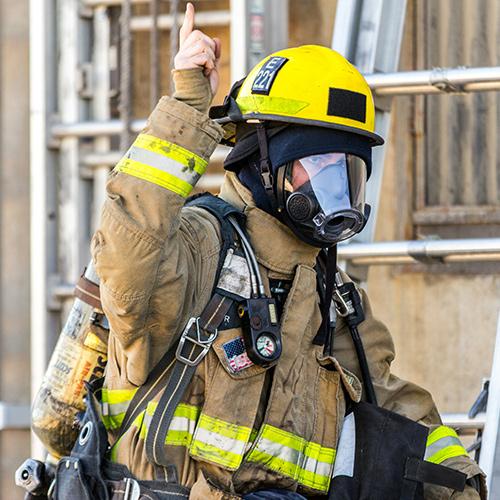 A firefighter in gear gets ready to climb a ladder.