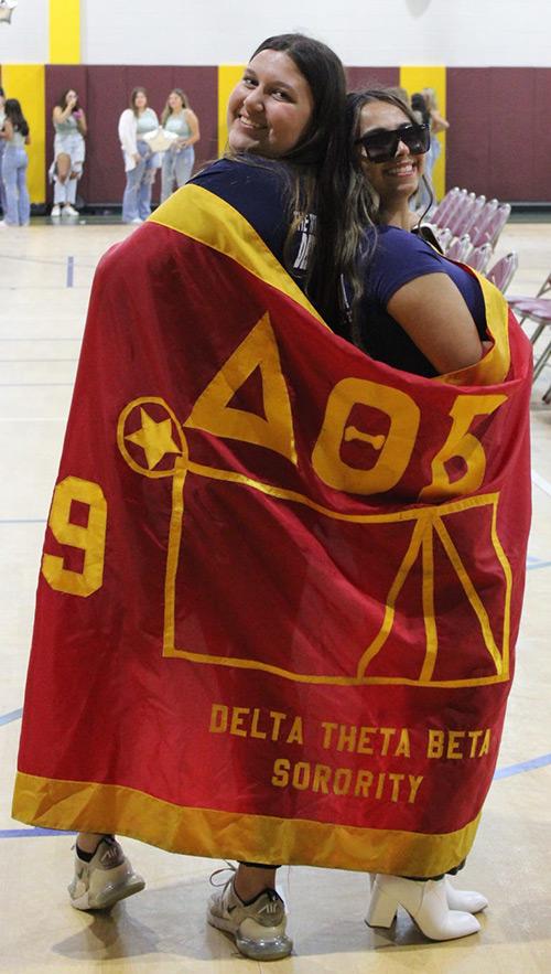 Two members of Delta Theta Beta wrapped in their banner.