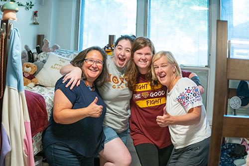 Two students move into their dorm with their moms and give the thumbs up.