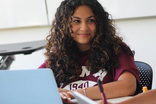 A student works at a laptop and smiles.