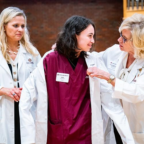 A professor puts a white coat on a nursing student.