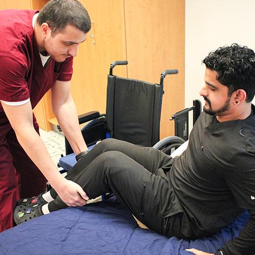 Two OT students practice assisting a client get into bed from a wheelchair.