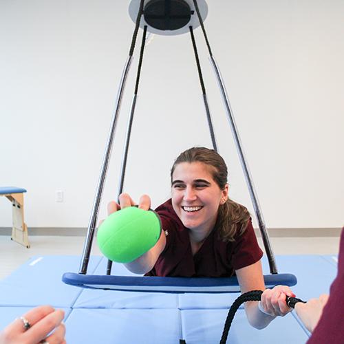 An OT student practices on a swing while grabbing a ball.