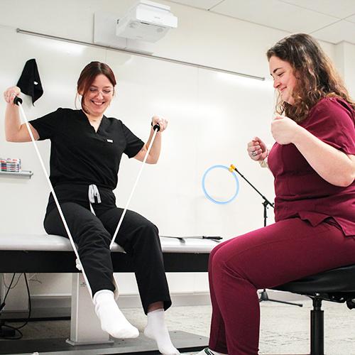 Two OT students practice assisting with putting on socks using a band.