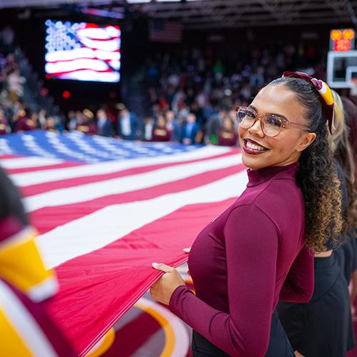 The cheer team holds up the flag at the home opener basketball game.