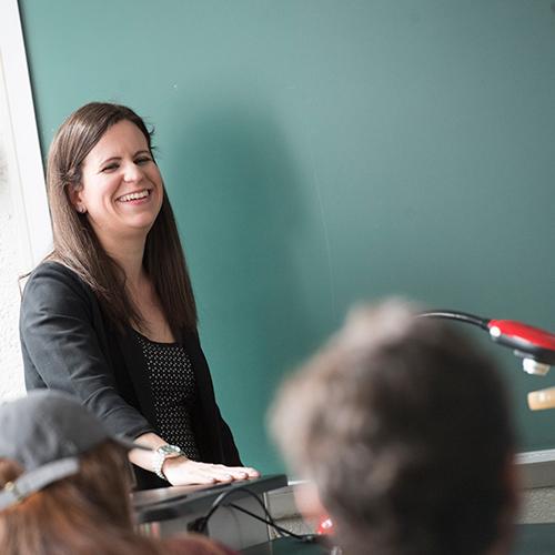 A teacher stands in front of a blackboard and smiles.