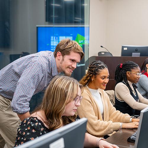 A computer science teacher helps students in the classroom.