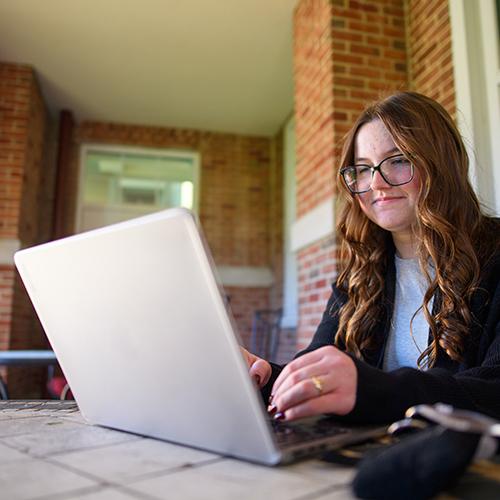 A student works on her laptop outside the library.