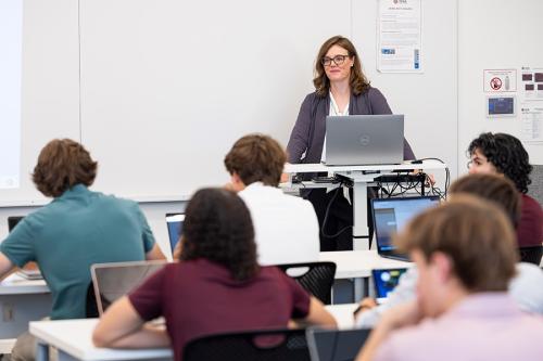 A teacher at the front of the class smiles.