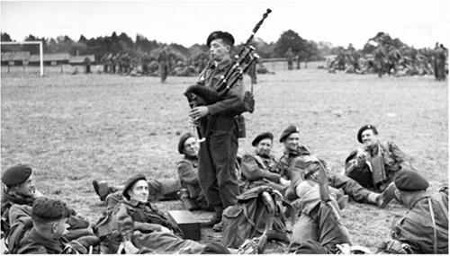 Bill Millin playing bagpipes with fellow soldiers around him.