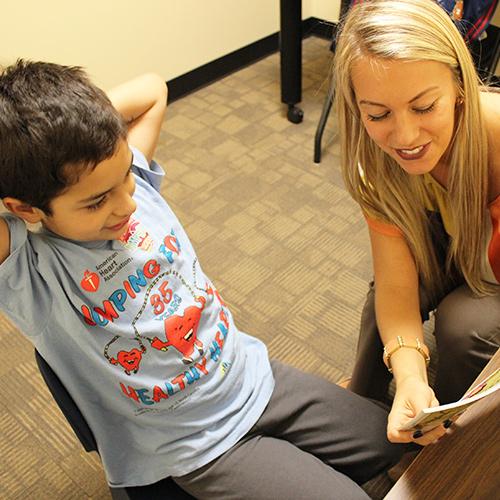 A speech language pathologist student works with a young boy out of a book.